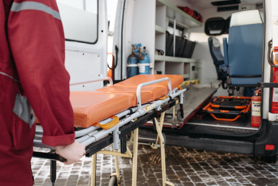 Inside the open rear of a commercial vehicle used for rubbish removal, a medical stretcher with an orange, waterproof cushion and white metal frame is positioned at the forefront, close to the vehicle